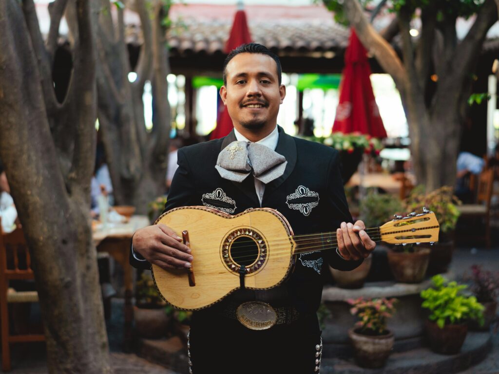 Portrait of a mariachi musician smiling while holding a guitar in a festive outdoor setting.