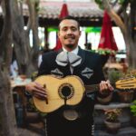 Portrait of a mariachi musician smiling while holding a guitar in a festive outdoor setting.